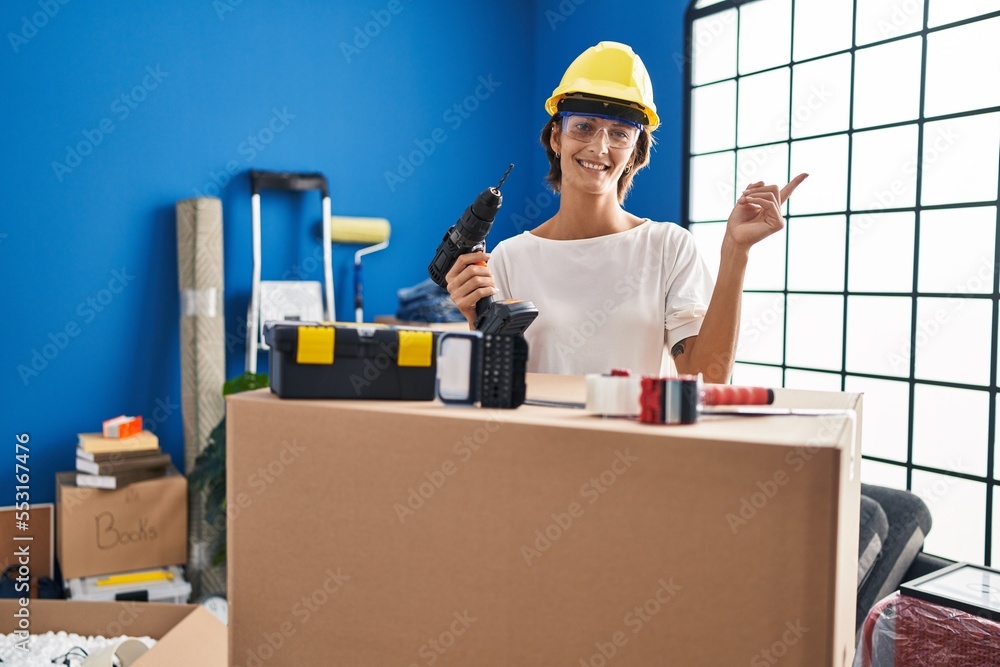 Brunette woman holding screwdriver at new home smiling happy pointing with hand and finger to the side Brunette woman holding screwdriver at new home smiling happy pointing with hand and finger to the side