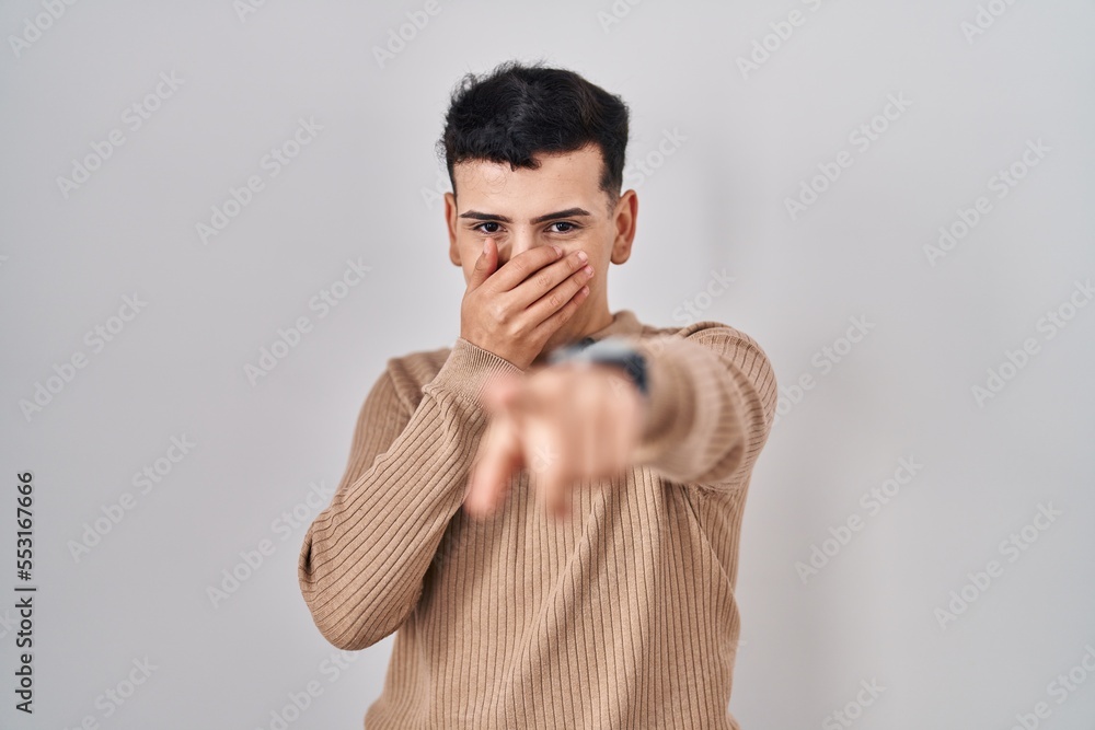 Non binary person standing over isolated background laughing at you, pointing finger to the camera with hand over mouth, shame expression Non binary person standing over isolated background laughing at you, pointing finger to the camera with hand over mouth, shame expression