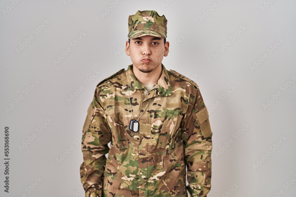 Young arab man wearing camouflage army uniform puffing cheeks with funny face. mouth inflated with air, crazy expression. Young arab man wearing camouflage army uniform puffing cheeks with funny face. mouth inflated with air, crazy expression.