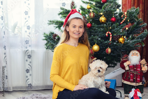 Happy woman surprised by her puppy dog Christmas gift sitting on the floor near Christmas tree