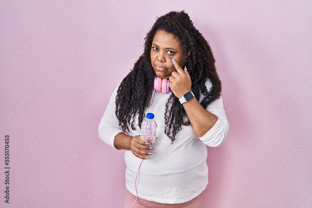 Plus size hispanic woman wearing sportswear and headphones pointing to the eye watching you gesture, suspicious expression Plus size hispanic woman wearing sportswear and headphones pointing to the eye watching you gesture, suspicious expression