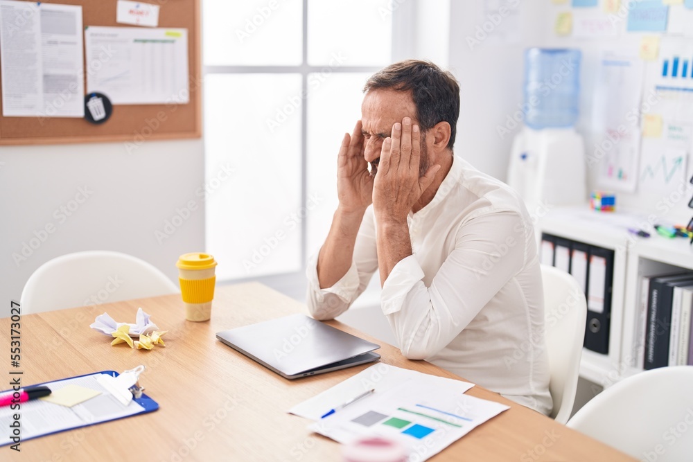 Middle age man business worker stressed sitting on tabl at office Middle age man business worker stressed sitting on tabl at office