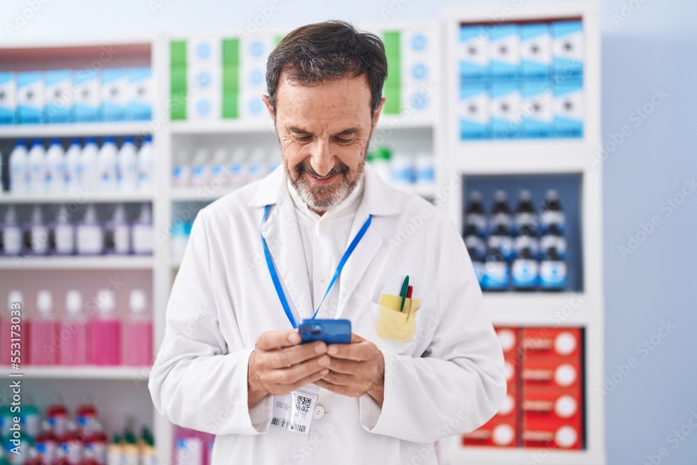 Middle age man pharmacist using smartphone working at pharmacy Middle age man pharmacist using smartphone working at pharmacy