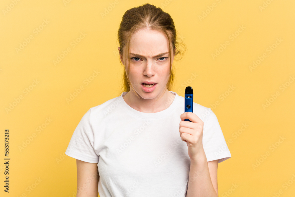 Young cute woman holding a vaper isolated on yellow background screaming very angry and aggressive. Young cute woman holding a vaper isolated on yellow background screaming very angry and aggressive.