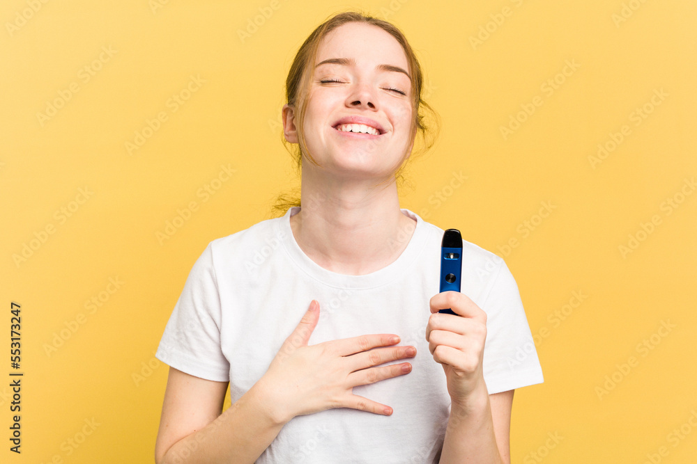 Young cute woman holding a vaper isolated on yellow background laughs out loudly keeping hand on chest. Young cute woman holding a vaper isolated on yellow background laughs out loudly keeping hand on chest.