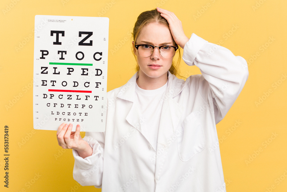 Young caucasian oculist woman holding a eye chart paper isolated on yellow background being shocked, she has remembered important meeting. Young caucasian oculist woman holding a eye chart paper isolated on yellow background being shocked, she has remembered important meeting.