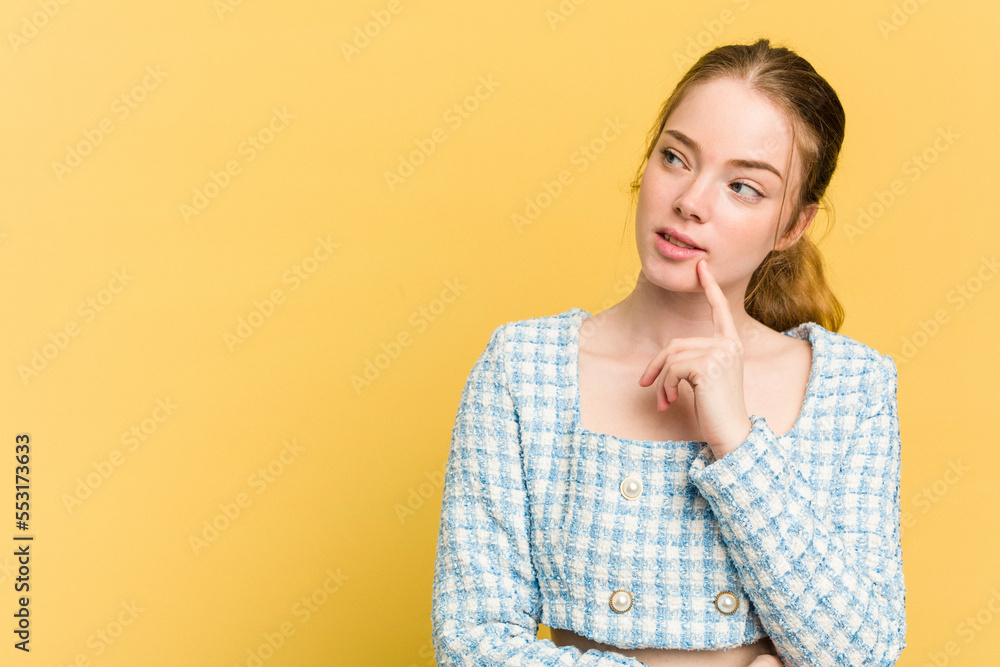 Young caucasian redhead woman isolated on yellow background looking sideways with doubtful and skeptical expression.