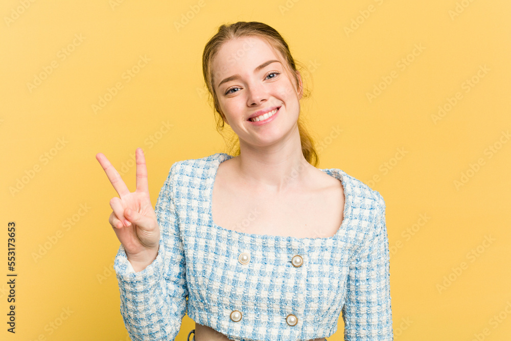 Young caucasian redhead woman isolated on yellow background showing victory sign and smiling broadly. Young caucasian redhead woman isolated on yellow background showing victory sign and smiling broadly.