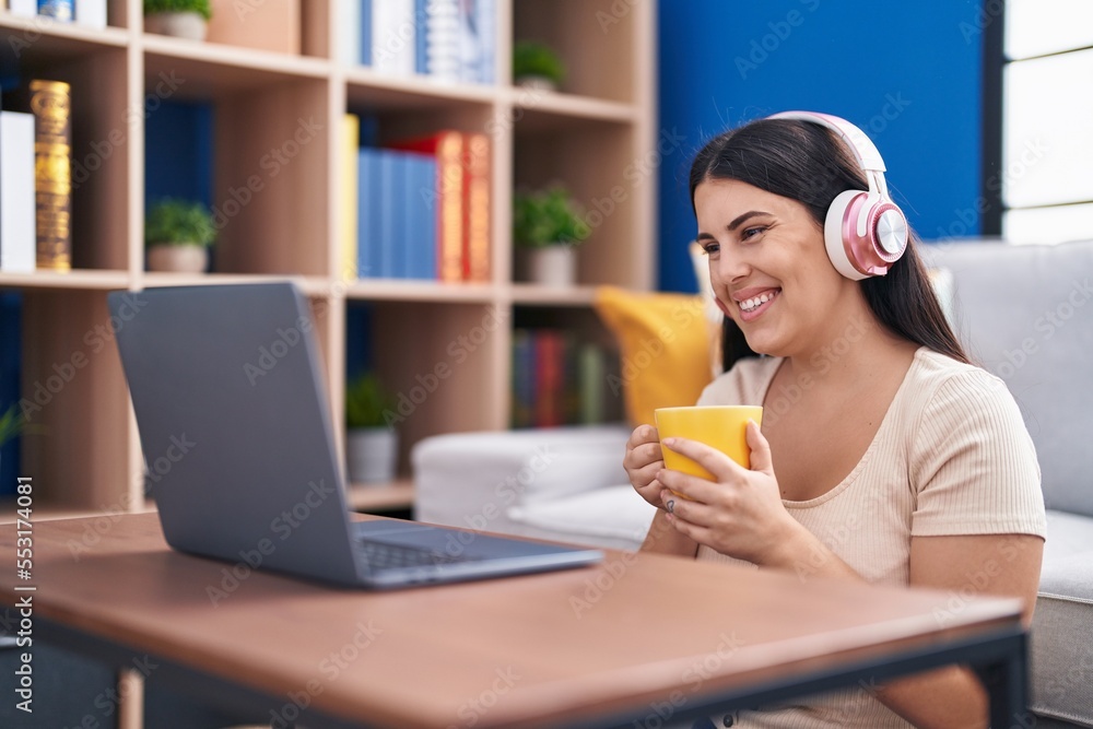 Young beautiful hispanic woman using laptop drinking coffee sitting on floor at home Young beautiful hispanic woman using laptop drinking coffee sitting on floor at home
