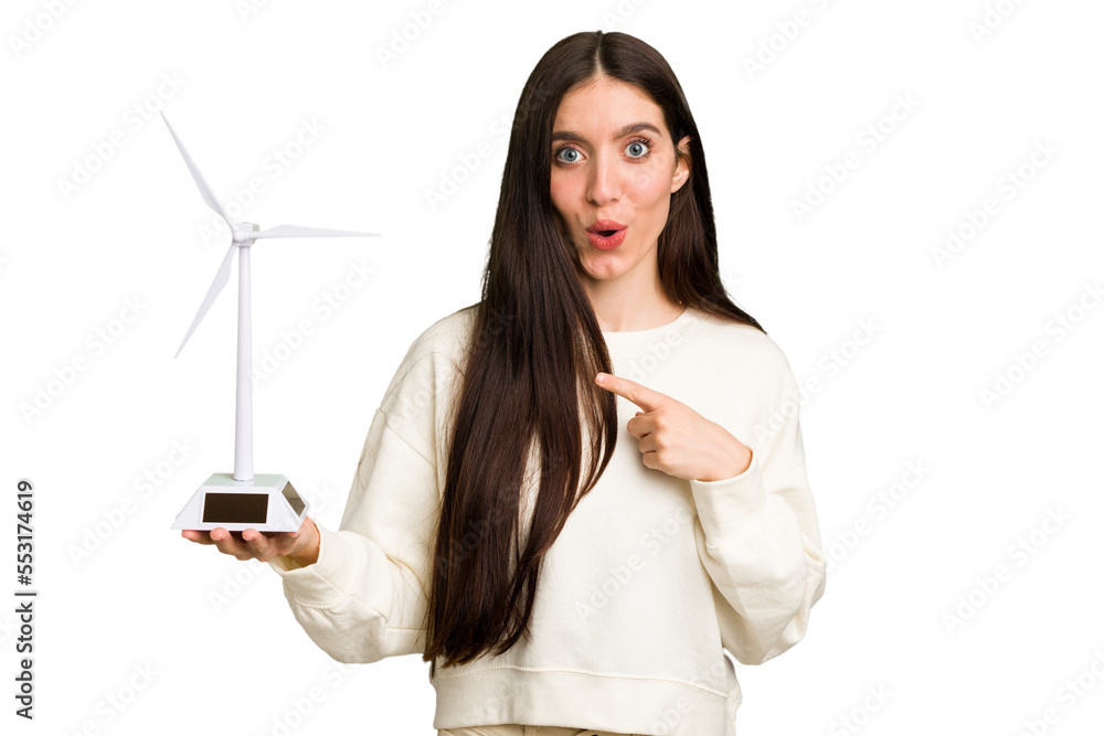 Young caucasian woman holding a small wind energy mill isolated pointing to the side Young caucasian woman holding a small wind energy mill isolated pointing to the side