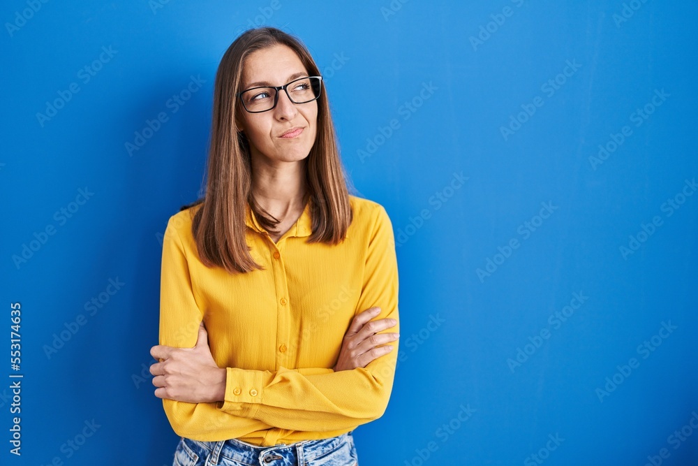 Obraz premium Young woman wearing glasses standing over blue background smiling looking to the side and staring away thinking.