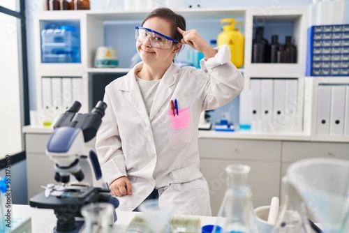 Hispanic girl with down syndrome working at scientist laboratory smiling pointing to head with one finger  great idea or thought  good memory
