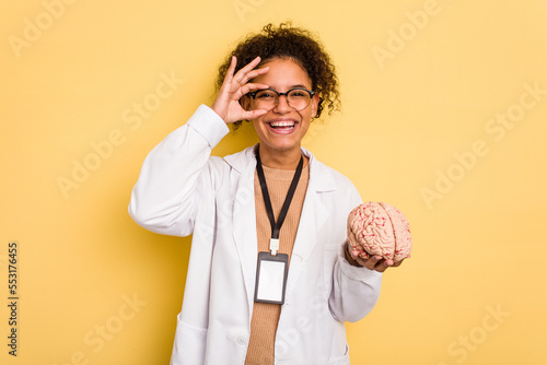 Young doctor brazilian woman holding a brain model isolated excited keeping ok gesture on eye.