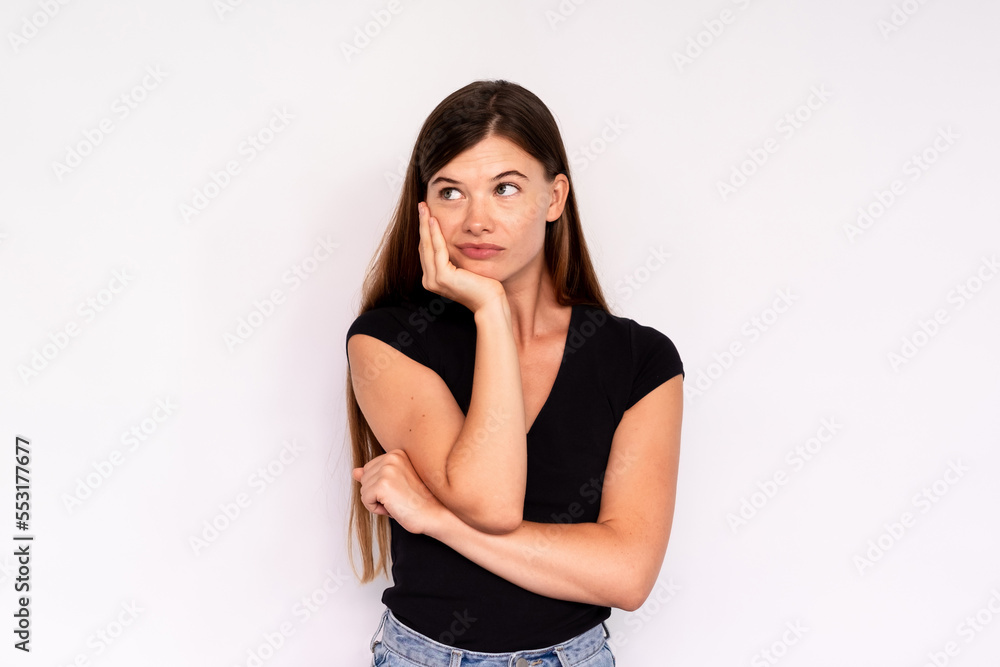 Portrait of bored young woman leaning head on hand over white background. Tired Caucasian lady wearing black T-shirt and jeans looking away. Boredom concept Portrait of bored young woman leaning head on hand over white background. Tired Caucasian lady wearing black T-shirt and jeans looking away. Boredom concept
