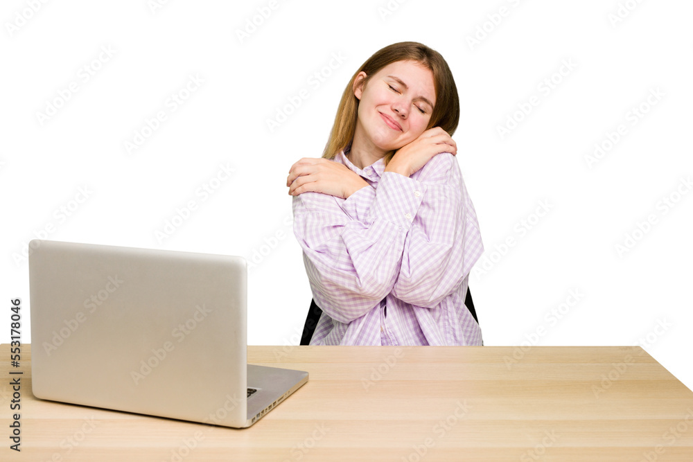 Young caucasian woman in a workplace working with a laptop isolated hugs, smiling carefree and happy. Young caucasian woman in a workplace working with a laptop isolated hugs, smiling carefree and happy.