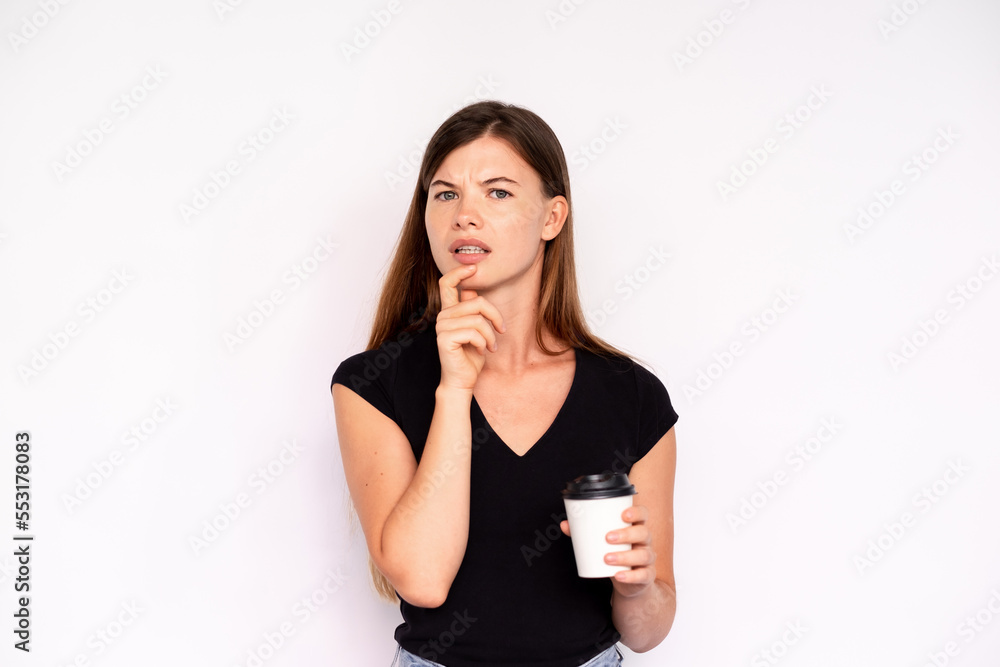 Portrait of incredulous young woman holding coffee over white background. Caucasian lady wearing black T-shirt looking at camera with doubtful expression. Doubt concept Portrait of incredulous young woman holding coffee over white background. Caucasian lady wearing black T-shirt looking at camera with doubtful expression. Doubt concept