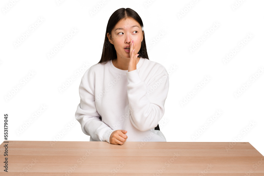 Young asian woman sitting on a table isolated is saying a secret hot braking news and looking aside Young asian woman sitting on a table isolated is saying a secret hot braking news and looking aside
