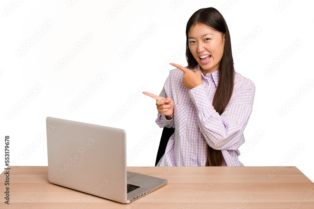 Young student asian woman in a workplace with a laptop isolated pointing with forefingers to a copy space, expressing excitement and desire. Young student asian woman in a workplace with a laptop isolated pointing with forefingers to a copy space, expressing excitement and desire.