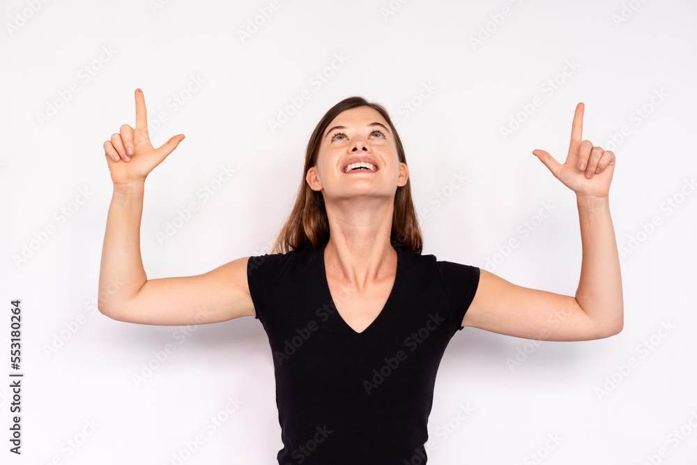 Portrait of excited young woman pointing upwards over white background. Caucasian lady wearing black T-shirt and jeans looking up and smiling. Advertising concept Portrait of excited young woman pointing upwards over white background. Caucasian lady wearing black T-shirt and jeans looking up and smiling. Advertising concept