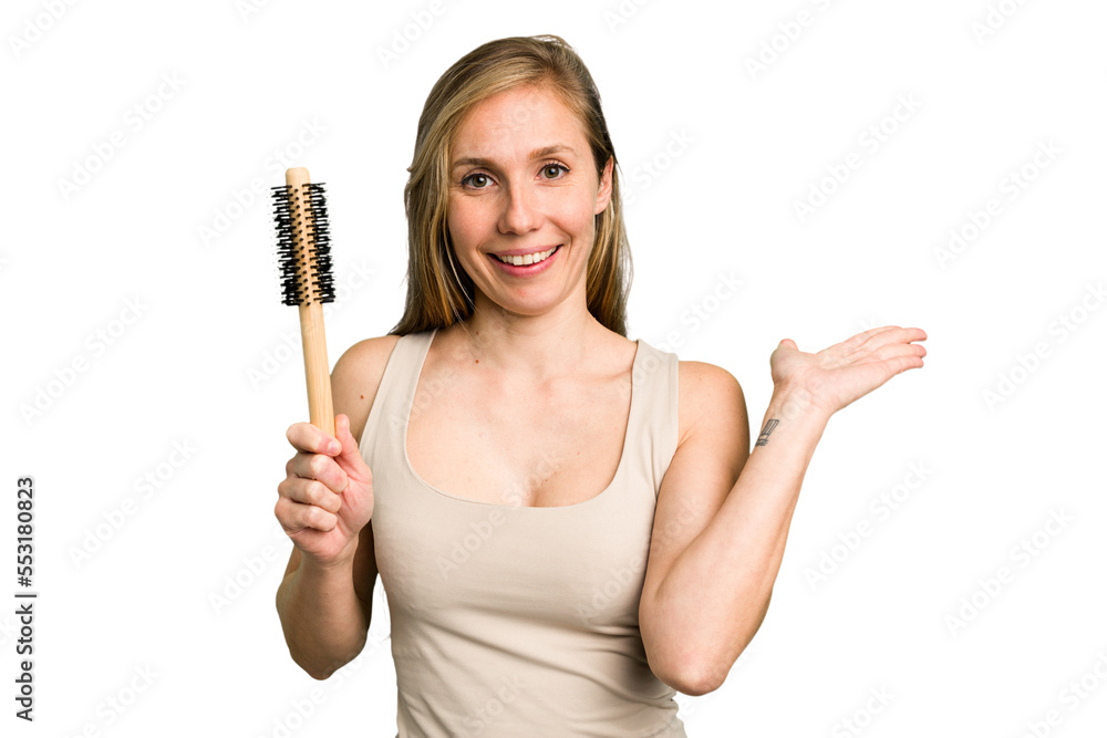Young caucasian woman using an hair comb isolated showing a copy space on a palm and holding another hand on waist. Young caucasian woman using an hair comb isolated showing a copy space on a palm and holding another hand on waist.