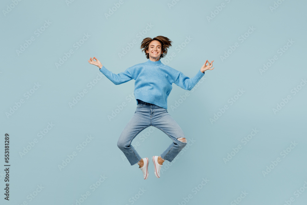 Full body spiritual young woman wear knitted sweater hold spreading hands in yoga om aum gesture relax meditate try to calm down isolated on plain pastel light blue cyan background studio portrait.