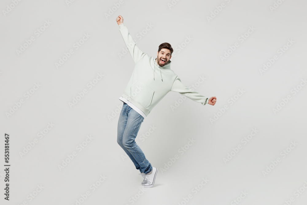 Full body happy young caucasian man wear mint hoody look camera stand on toes leaning back with outstretched hands isolated on plain solid white background studio portrait. People lifestyle concept. Full body happy young caucasian man wear mint hoody look camera stand on toes leaning back with outstretched hands isolated on plain solid white background studio portrait. People lifestyle concept.