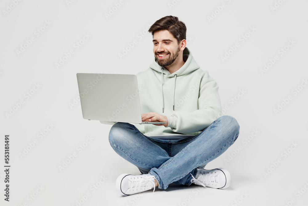 Full body smiling happy programmer smart young caucasian IT man wear mint hoody hold use work on laptop pc computer isolated on plain solid white background studio portrait. People lifestyle concept. Full body smiling happy programmer smart young caucasian IT man wear mint hoody hold use work on laptop pc computer isolated on plain solid white background studio portrait. People lifestyle concept.