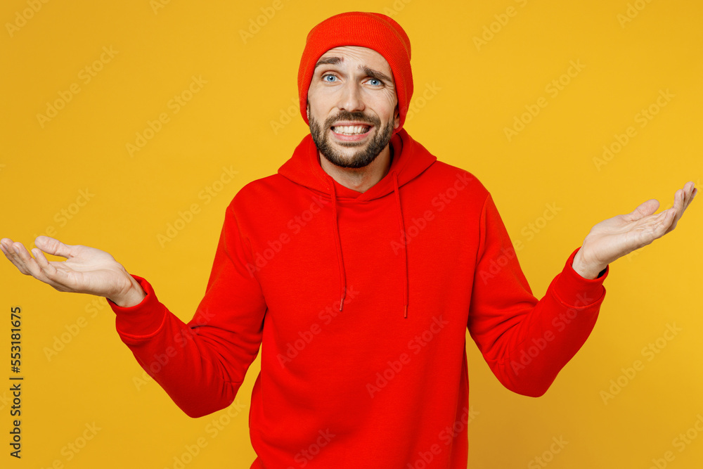 Young caucasian man in red hoody hat spread hnads shrugging shoulders looking puzzled, have no idea, nothing to say isolated on plain yellow color background studio portrait People lifestyle concept Young caucasian man in red hoody hat spread hnads shrugging shoulders looking puzzled, have no idea, nothing to say isolated on plain yellow color background studio portrait People lifestyle concept