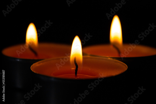 Composition of three candles on dark luxury night background. Black table, side view. Candles Burning at Night. Orange taper burning in focus, foreground. illustration design.