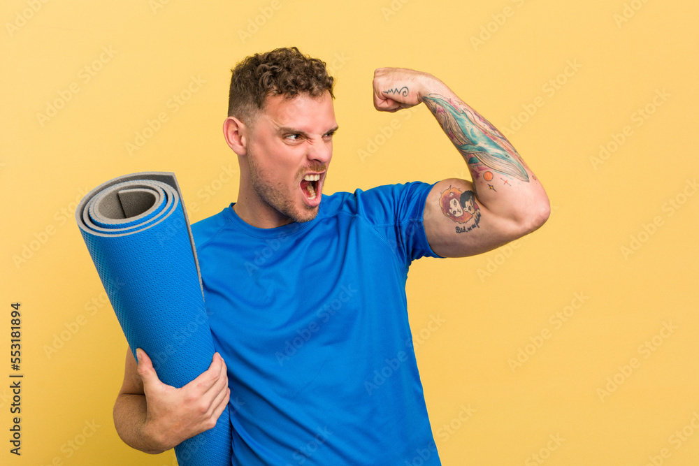 Φωτογραφία Young caucasian sport man holding a mat isolated on yellow background raising fist after a victory, winner concept
