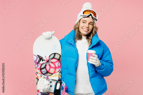 Snowboarder woman wear blue suit goggles mask hat ski padded jacket hold takeaway paper cup coffee to go look aside isolated on plain pink background. Winter extreme sport hobby weekend trip concept.