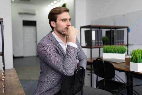 a business man in a jacket sits on a chair in the office, thinking, looks ahead