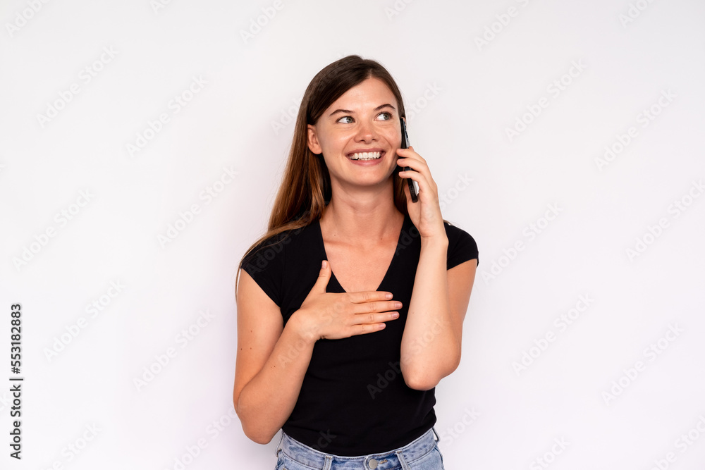 Portrait of cheerful young woman talking on mobile phone over white background. Caucasian lady wearing black T-shirt and jeans looking away and smiling. Mobile communication concept Portrait of cheerful young woman talking on mobile phone over white background. Caucasian lady wearing black T-shirt and jeans looking away and smiling. Mobile communication concept