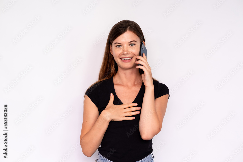 Portrait of happy young woman talking on mobile phone over white background. Caucasian lady wearing black T-shirt and jeans calling friend. Mobile communication concept