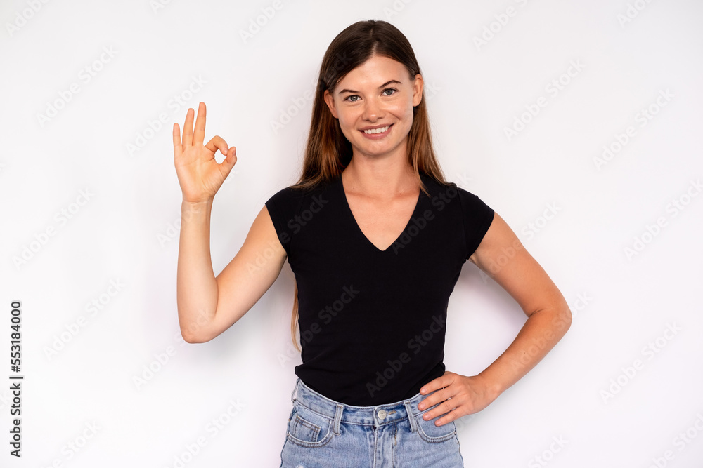 Portrait of happy young woman making ok gesture over white background. Caucasian lady wearing black T-shirt and jeans showing done sign and smiling at camera. Success and satisfaction concept Portrait of happy young woman making ok gesture over white background. Caucasian lady wearing black T-shirt and jeans showing done sign and smiling at camera. Success and satisfaction concept