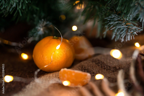 tangerine, tangerine slices on a warm classic plaid. cozy atmosphere with glowing lights and Christmas tree branches. winter background.