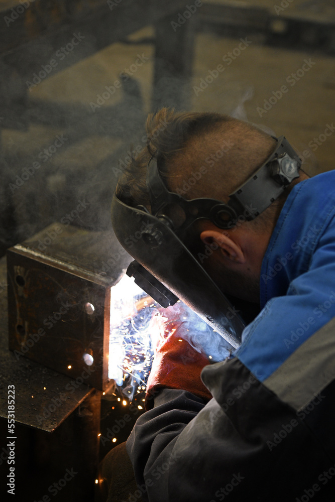A worker welding metal parts on a construction site. A welder welds parts of a large machine in a metallurgical workshop.. An interesting example of manual work. A worker welding metal parts on a construction site. A welder welds parts of a large machine in a metallurgical workshop.. An interesting example of manual work.