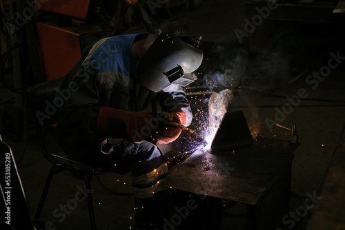 A worker welding metal parts on a construction site. A welder welds parts of a large machine in a metallurgical workshop.. An interesting example of manual work.  © Cveja