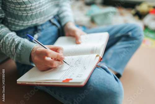 Free time you need to do something, woman unrecognizable sits on floor of room, in chair, writes in notebook. Lot of things have accumulated you need to write down in diary so as not to forget.