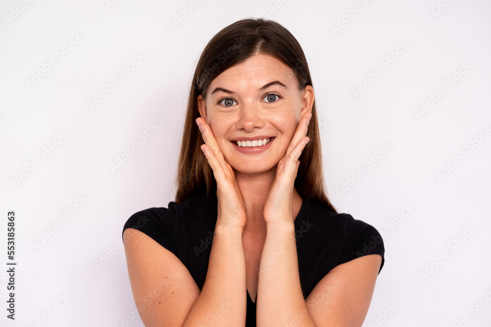 Portrait of happy young woman touching face and looking at camera over white background. Caucasian lady wearing black T-shir smiling at camera. Female beauty concept Portrait of happy young woman touching face and looking at camera over white background. Caucasian lady wearing black T-shir smiling at camera. Female beauty concept