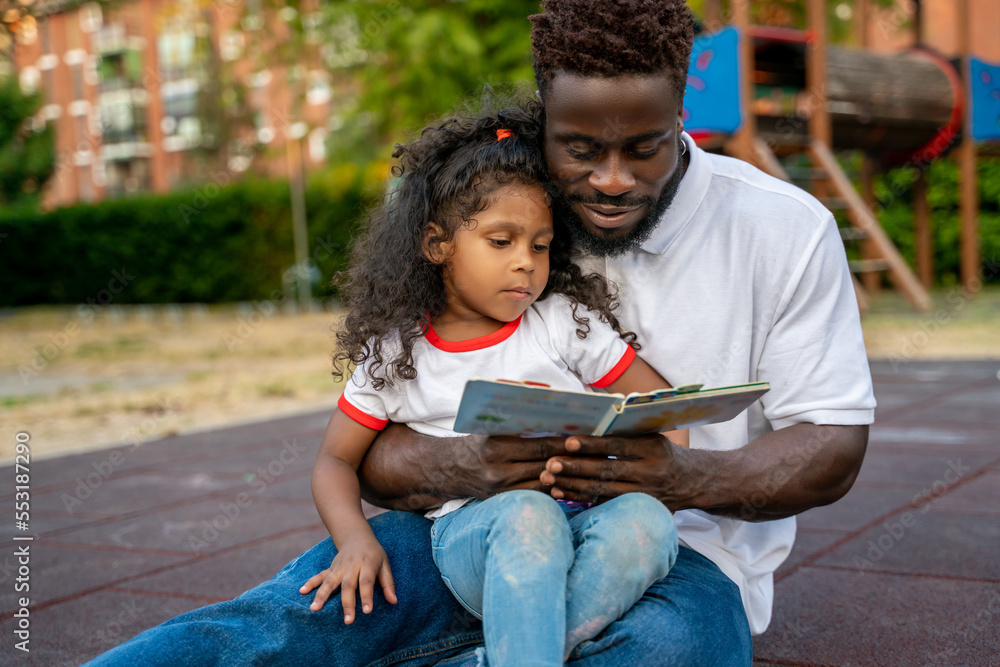 Young man and a little girl reading a book together and looking involved Young man and a little girl reading a book together and looking involved