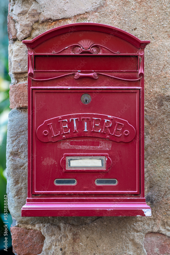 Traditional red colored old mailbox hanging on the wall in Italian countryside.