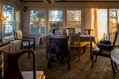Broomes island, Maryland USA A senior woman in a wheelchasir sits in the living room of a country house with big windows.