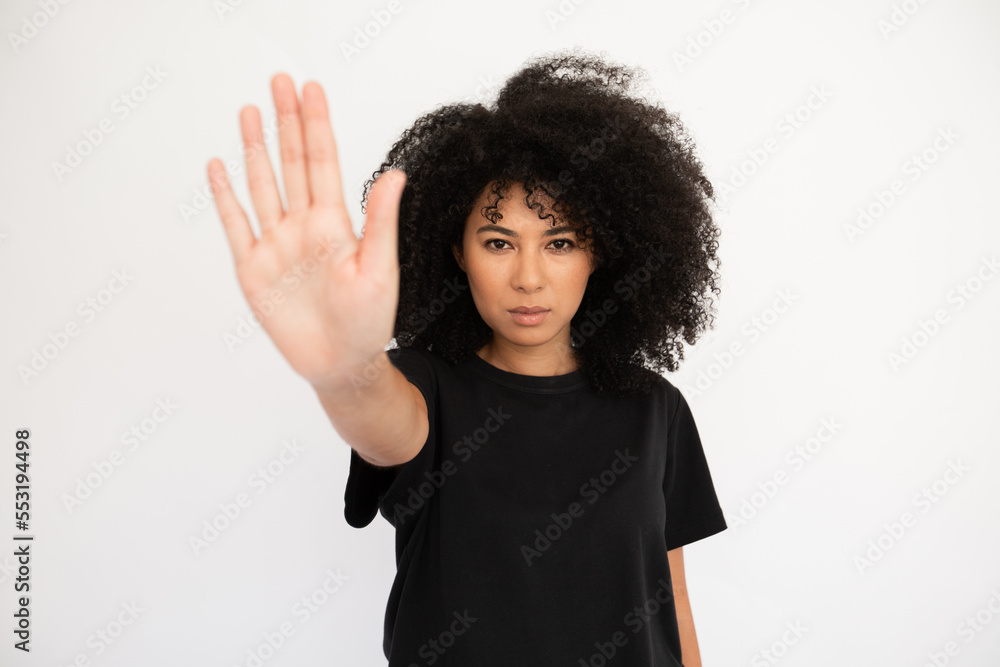 Serious young woman showing stop sign. Caucasian female model with afro hairstyle and brown eyes in black T-shirt showing her palm as stop sign. Forbiddance, advertising concept Serious young woman showing stop sign. Caucasian female model with afro hairstyle and brown eyes in black T-shirt showing her palm as stop sign. Forbiddance, advertising concept