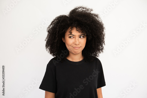 Confused woman showing doubt. Hispanic female model with afro hairstyle and brown eyes in casual clothes feeling unsure making decision. Hesitation, thought concept © KAMPUS