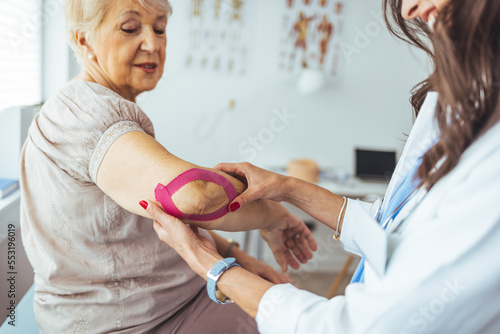Female doctor chiropractor or osteopath fixing womans shoulder with hands movements during visit in manual therapy clinic. Support for strained muscles.  Physical therapy diagnosing concept