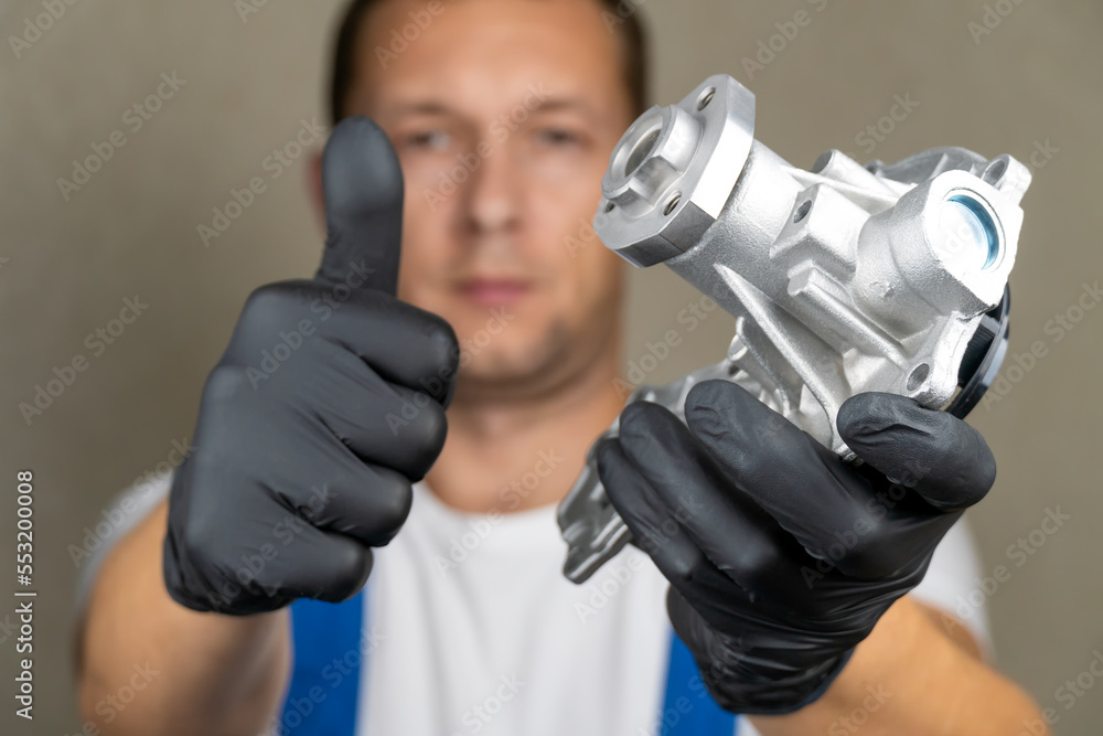 Car mechanic in blue jumpsuit holds water pump for cooling in his hands
