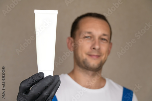 Employee in blue uniform and white T-shirt holds white tube on which you can place logo or text. Space for copying.