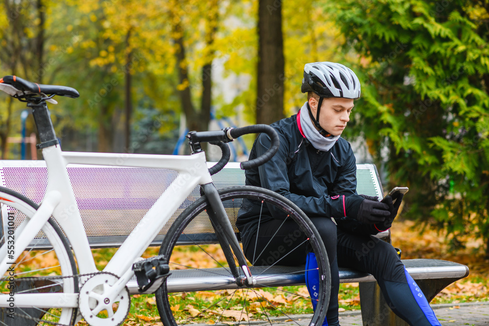 Fototapeta premium Young bicyclist relax with smartphone in park