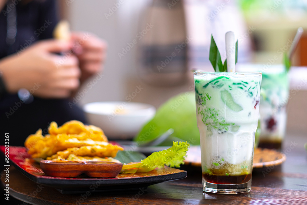 Es cendol is a traditional Indonesian iced dessert. Popular during fasting in Ramadan. A refreshing cold drink when drunk in the day and evening. A woman eating tempe as a bokeh background. Es cendol is a traditional Indonesian iced dessert. Popular during fasting in Ramadan. A refreshing cold drink when drunk in the day and evening. A woman eating tempe as a bokeh background.
